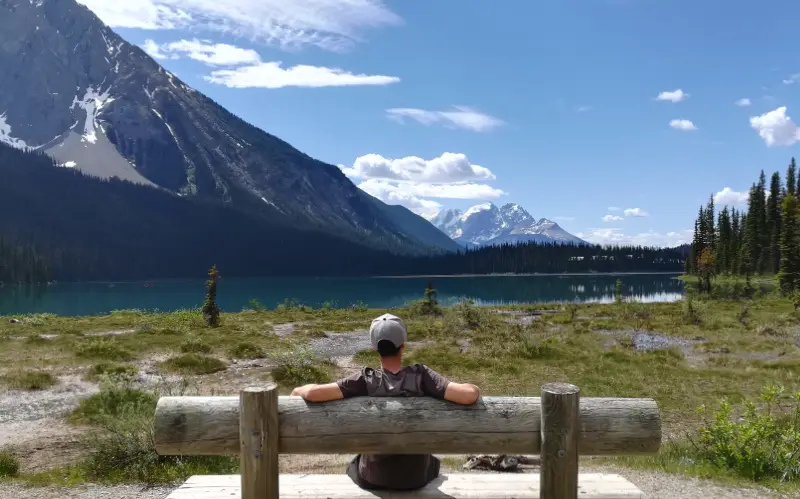 Viajero sentado en un banco de madera contemplando Emerald Lake y las montañas nevadas desde la ruta circular, Yoho