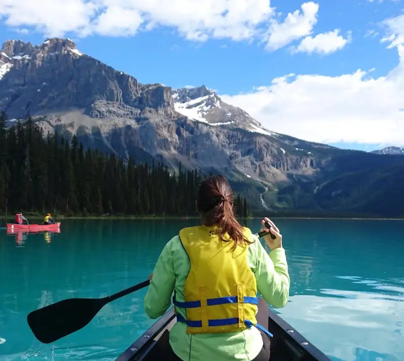 Persona remando en canoa por Emerald Lake con chaleco salvavidas amarillo, aguas turquesas y montañas nevadas al fondo