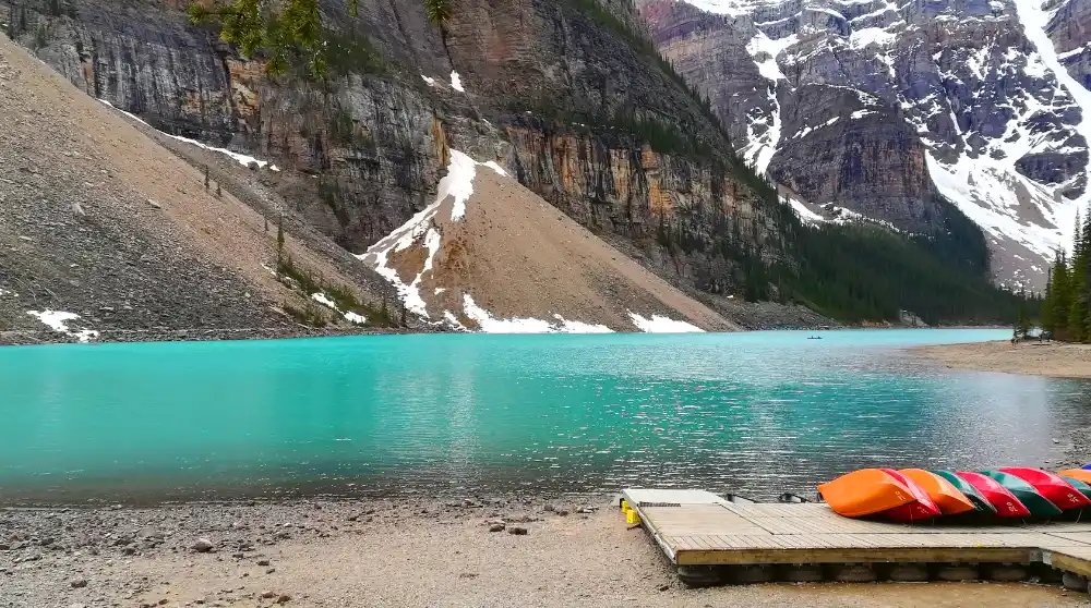 Canoas de colores rojo, naranja y verde alineadas en el embarcadero de madera junto a las aguas turquesas del lago Moraine.
