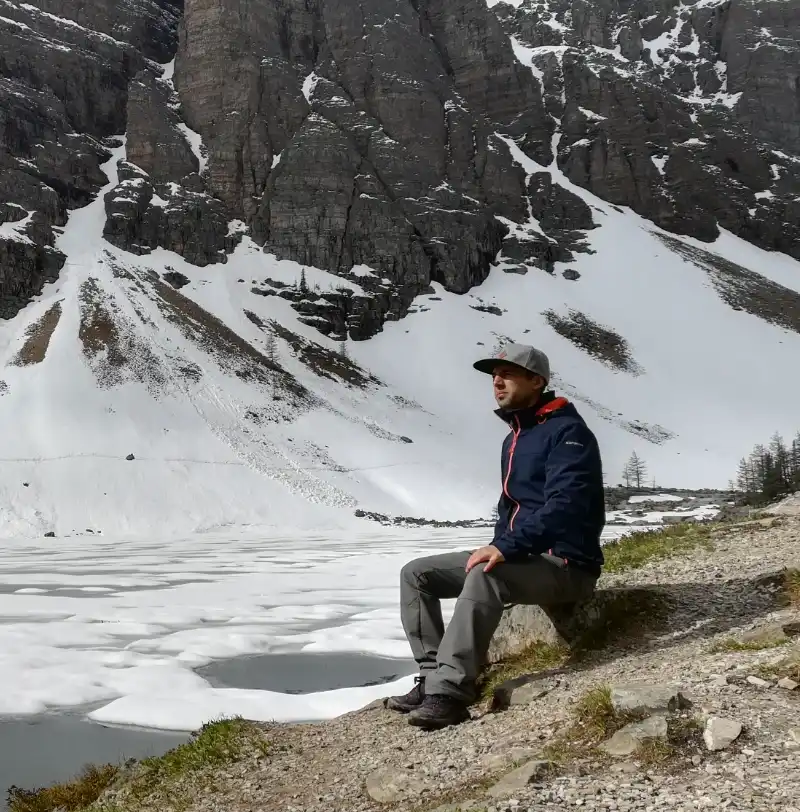 Senderista sentado en una roca contemplando el lago Agnes helado y las montañas nevadas del Parque Nacional Banff.