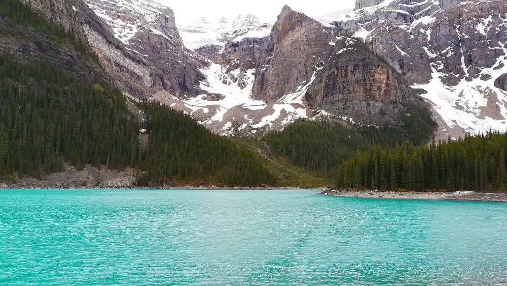 Vista amplia del lago Moraine rodeado de densos bosques de pinos y montañas escarpadas con glaciares en el Parque Nacional Banff.