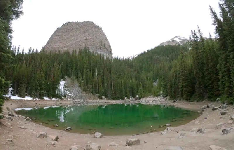 El lago Mirror Lake reflejando el Big Beehive bajo un cielo nublado en la ruta de senderismo hacia Lake Agnes.