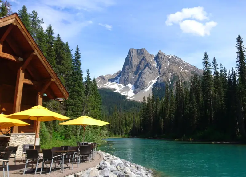 Terraza del Emerald Lake Lodge con sombrillas amarillas junto al lago turquesa y una montaña rocosa al fondo, Yoho