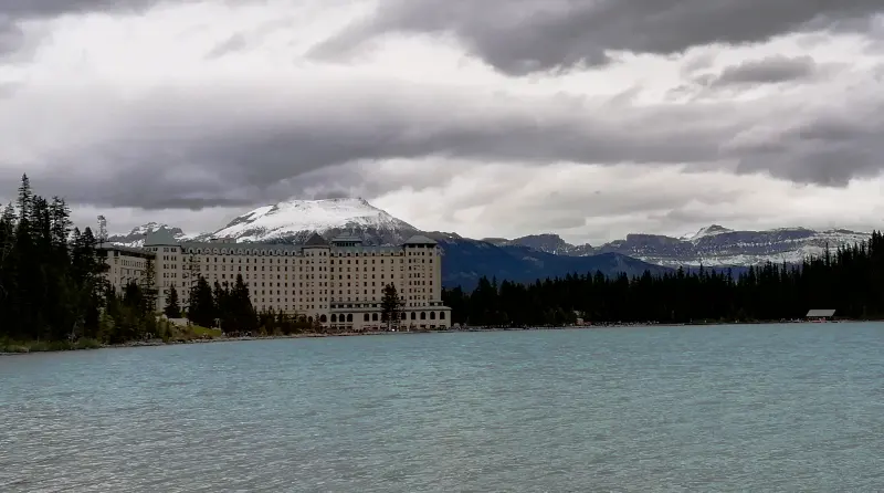 Fachada del hotel Fairmont Château Lake Louise visto desde el paseo de la orilla (Lakeshore) con montañas nevadas al fondo.