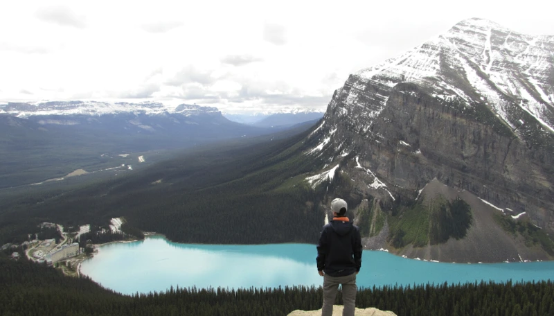 Persona contemplando las vistas panorámicas de Lake Louise y el hotel Fairmont desde la cima de un mirador en las Rocosas Canadienses.