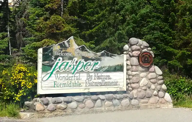 Cartel de madera y piedra de bienvenida al Parque Nacional Jasper con el lema "Wonderful by Nature" rodeado de bosque.