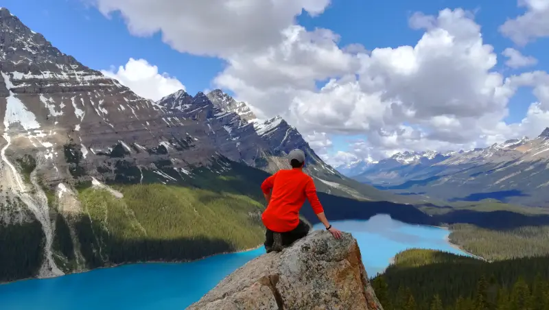 Persona sentada en una roca en el mirador no oficial de Peyto Lake, disfrutando de una vista panorámica sin vallas del lago turquesa y el valle.