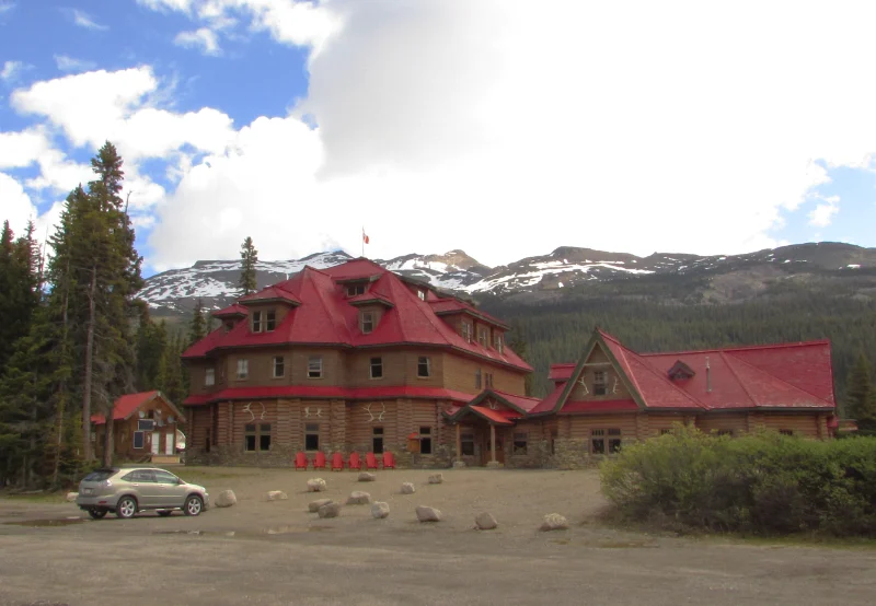 Vista exterior del edificio principal de madera con tejado rojo de The Lodge at Bow Lake frente a las montañas nevadas.