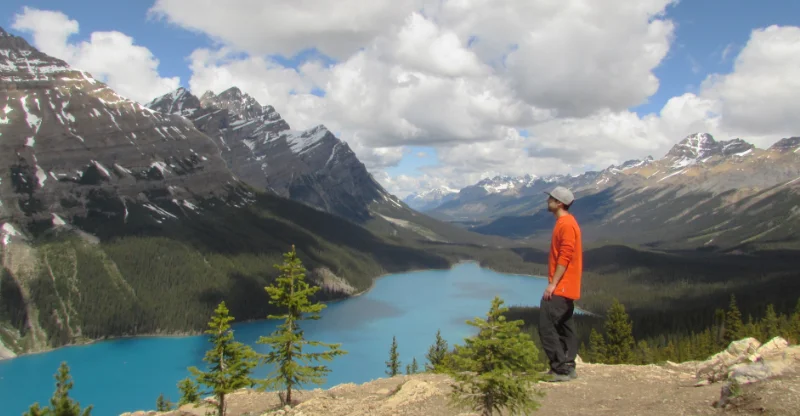 Hombre de pie en el borde del mirador de Peyto Lake observando el lago con forma de lobo y las montañas de las Rocosas Canadienses.
