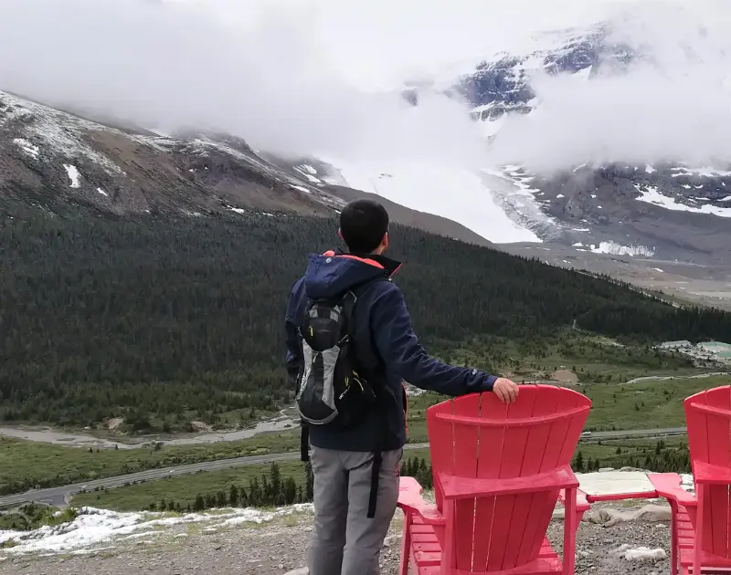 Jokin junto a las icónicas sillas rojas de Parks Canada en Wilcox Pass con vistas panorámicas al Glaciar Athabasca.