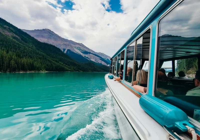 Vista lateral desde el barco de un crucero navegando por las intensas aguas turquesas del lago Maligne, rodeado de bosques de pinos y montañas en Jasper.